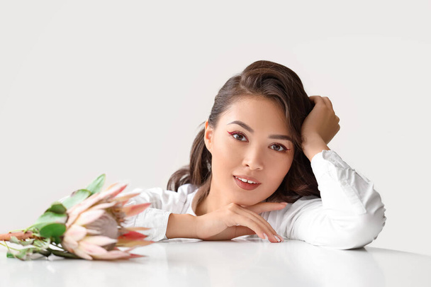 Jeune femme asiatique avec belle fleur de protéa à table près du mur blanc - Photo, image