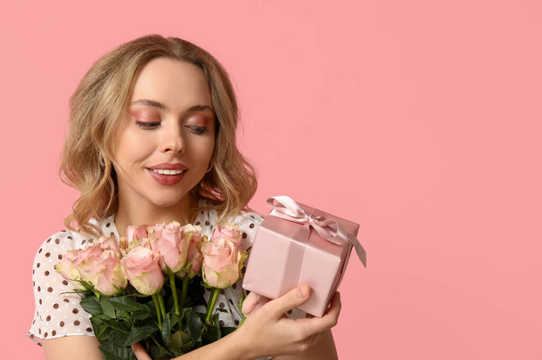 Young woman with bouquet of beautiful roses and gift box on pink background - Photo, Image