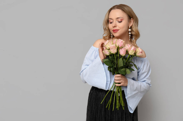 Hübsche junge Frau mit einem Strauß schöner Rosen auf grauem Hintergrund - Foto, Bild