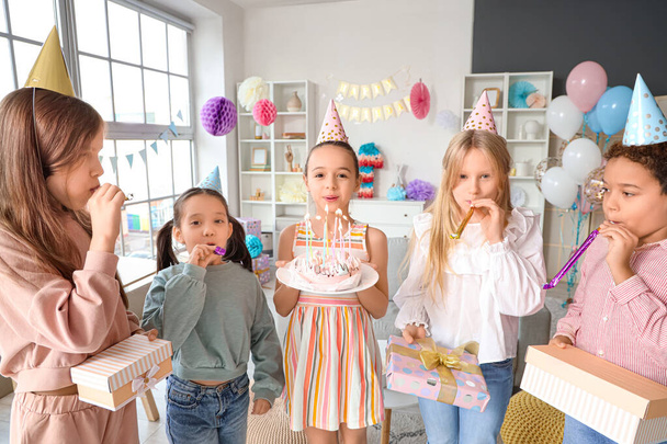 Cute little girl blowing out candles on Birthday cake with her friends at home party - Photo, Image