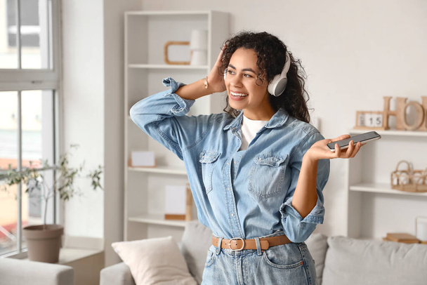 Joven mujer afroamericana en auriculares con teléfono móvil escuchando música en casa - Foto, imagen