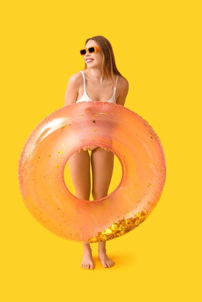 Mujer bastante joven en traje de baño de tanque y con anillo inflable sobre fondo amarillo - Foto, imagen