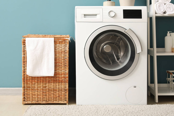 Rieten mand en wasmachine in de buurt van blauwe muur in wasruimte - Foto, afbeelding