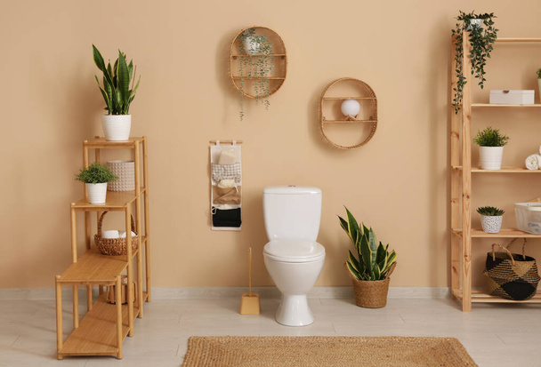 Interior of stylish bathroom with houseplants and ceramic toilet bowl near beige wall - Photo, Image