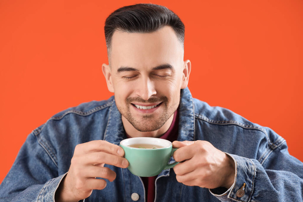 Bonito homem com xícara de chá no fundo laranja, close-up - Foto, Imagem