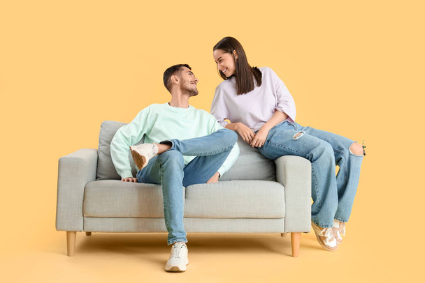 Beautiful young happy couple spending time together on sofa against yellow background - Photo, Image