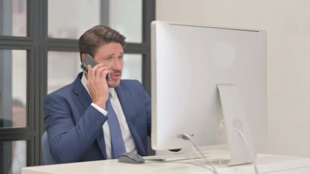 Сердитий середнього віку бізнесмен розмовляє по телефону під час роботи на робочому столі - Кадри, відео