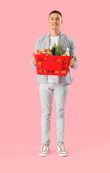Fiatal férfi teljes bevásárló kosár rózsaszín háttér - Fotó, kép