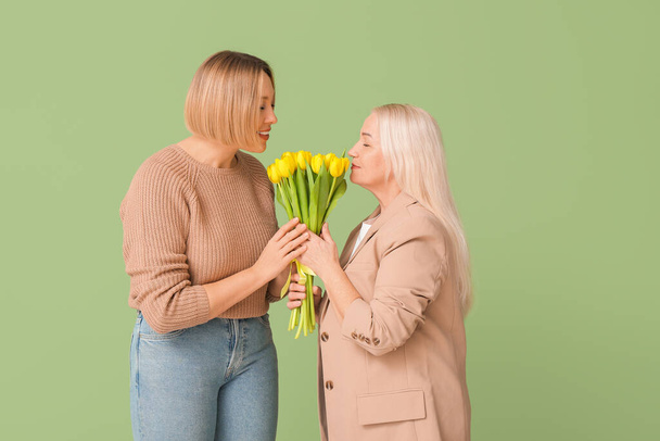 Взрослая женщина приветствует свою мать букетом тюльпанов на зеленом фоне. Международный женский день - Фото, изображение