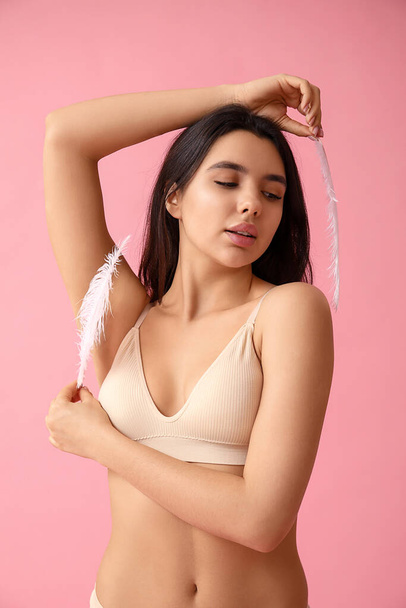 Pretty young woman with soft feathers on pink background. Epilation concept - Photo, Image