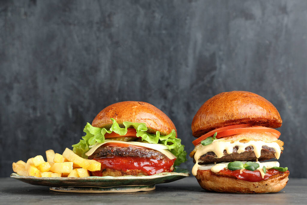 Тарелка с вкусными гамбургерами и картошкой фри на сером фоне гранжа - Фото, изображение