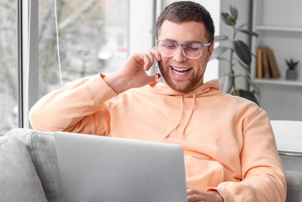 Portret van een mannelijke programmeur met laptop in gesprek via de telefoon op de bank op kantoor - Foto, afbeelding