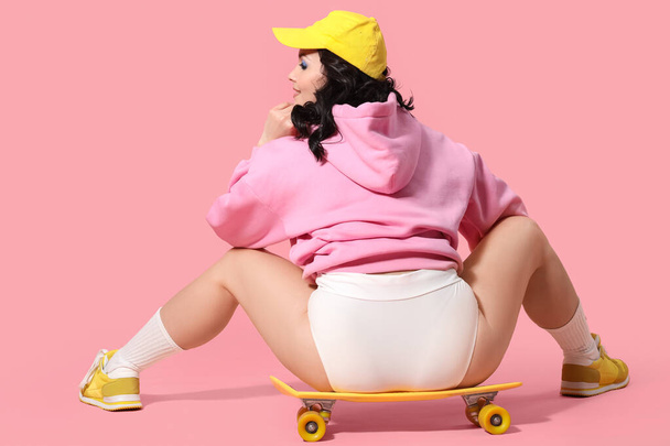 ピンクの背景にスケートボードとスタイリッシュな下着で美しい若いボディ肯定的な女性 - 写真・画像