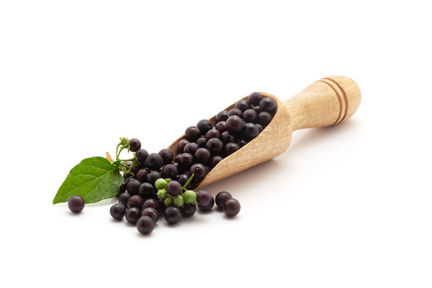 Vista frontal de una cucharada de madera llena de crema negra orgánica fresca o fruta Makoy (Solanum nigrum). Aislado sobre un fondo blanco. - Foto, Imagen