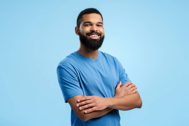 Щасливий бородатий афроамериканський чоловік позує в студії зі схрещеними руками, дивлячись на камеру, ізольований на синьому фоні. Концепція способу життя людей - Фото, зображення