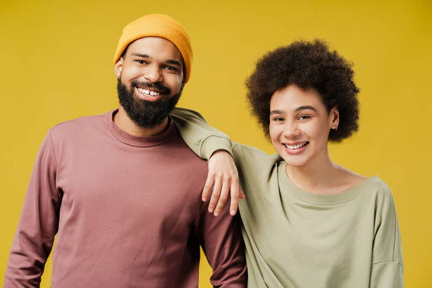 Smiling African American woman leaning on male shoulder, posing in studio together, isolated on yellow background. Lifestyle people concept - Fotoğraf, Görsel