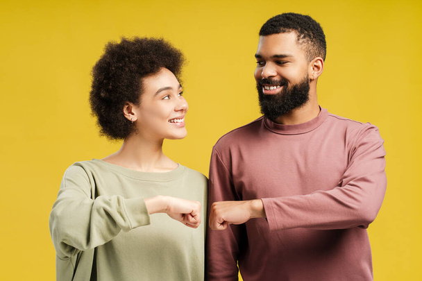 Smiling African American man and woman making fist bumps, working as team in studio, isolated on yellow background. Lifestyle people concept - Photo, Image