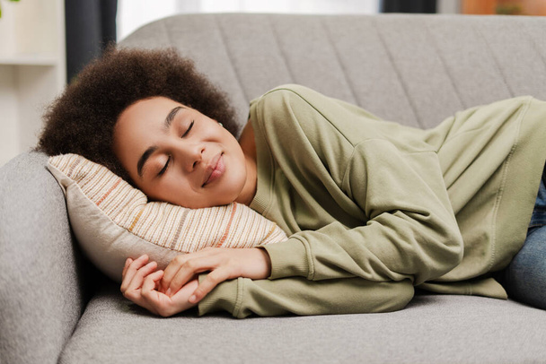 アフリカ系アメリカ人の若い女性は,自宅のソファーに横たわりながら寝ている. 人,休息,快適さ,レジャーのコンセプト - 写真・画像