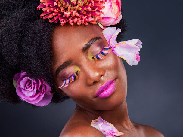 African, girl and beauty with flowers, makeup and confidence for lashes, skincare and wellness in studio. Female person, art and pride for creative, style and luxury in grey background for cosmetics. - Photo, Image