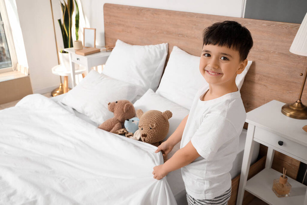 Schattig gelukkig jongetje met speelgoed maken bed in slaapkamer - Foto, afbeelding
