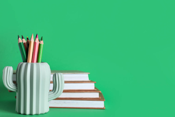 Potloodhouder met potloden en boeken op groene ondergrond - Foto, afbeelding