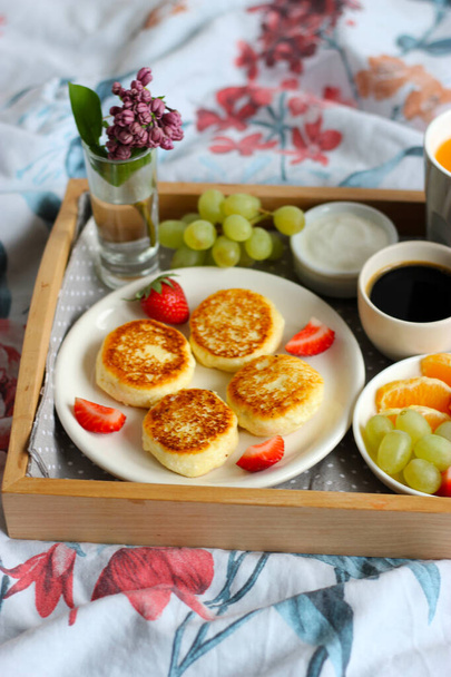Desayuno en la cama - tartas de queso cottage con café negro, jugo de naranja, crema agria y frutas frescas - Foto, imagen