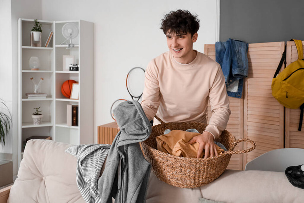 Estudiante masculino recogiendo ropa en la cesta en casa - Foto, imagen