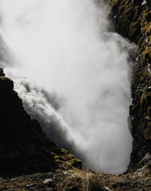 Bir şelale kayalık bir uçurumdan aşağı su döküyor. Su beyaz ve sisli, sakin ve huzurlu bir atmosfer yaratıyor. Altın Çember, İzlanda. - Fotoğraf, Görsel