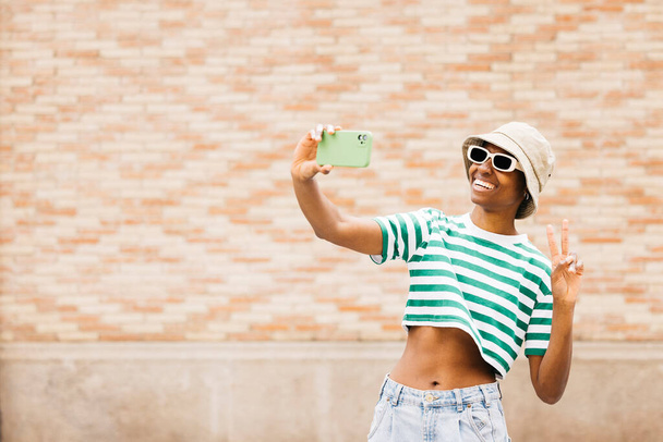 Ulkona muotokuva nuori iloinen nainen aurinkolasit ja hattu ja ottaa selfie. Nuori nainen hymyilee iloisesti ulkona. - Valokuva, kuva