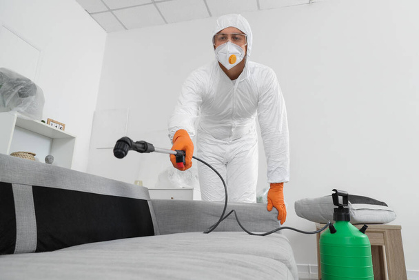 Male worker disinfecting sofa in room - Photo, Image