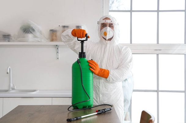 Male worker with disinfectant cylinder at table in kitchen - Photo, Image