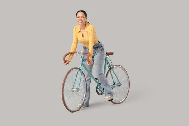 Όμορφη νεαρή γυναίκα ιππασία ποδήλατο σε γκρι φόντο - Φωτογραφία, εικόνα
