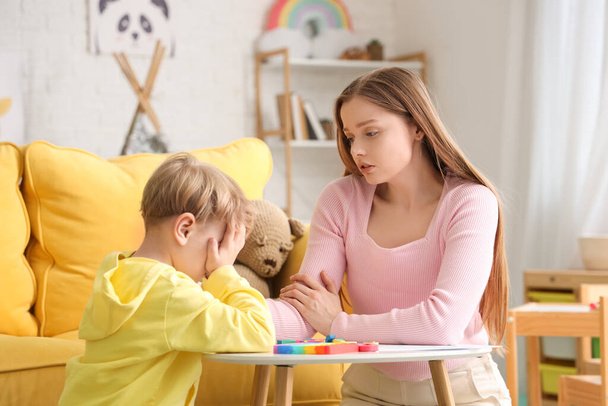 Female psychologist working with stressed little boy at table in office. World Autism Awareness Day - Photo, Image