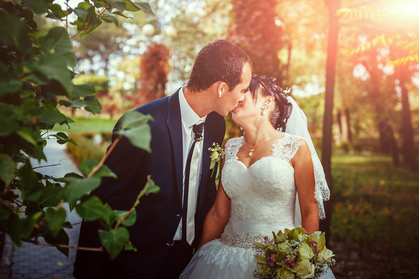 Young couple kissing in wedding gown. Bride holding bouquet of flowers - Foto, Bild