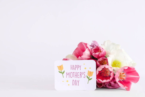 Pozdrav s textem Šťastný den matek a krásné tulipány na bílém pozadí - Fotografie, Obrázek