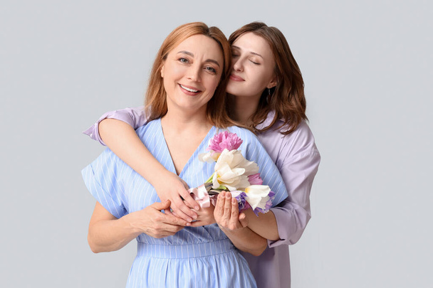 Kaunis kypsä nainen kukkakimppu tulppaanit ja hänen tyttärensä harmaalla taustalla. Äitienpäivän juhla - Valokuva, kuva