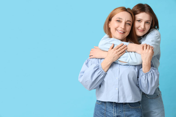 Hermosa mujer madura con su hija abrazándose sobre fondo azul. Celebración del Día de la Madre - Foto, Imagen