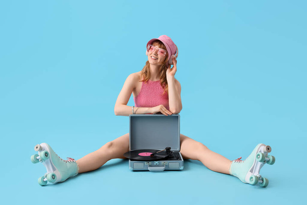 Young happy woman in roller skates with record player and vinyl disk on blue background - Photo, Image
