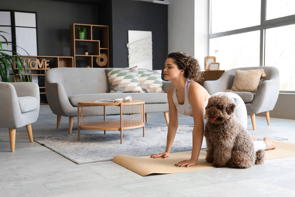 Sportliche junge Frau mit süßem Pudel beim Yoga zu Hause - Foto, Bild