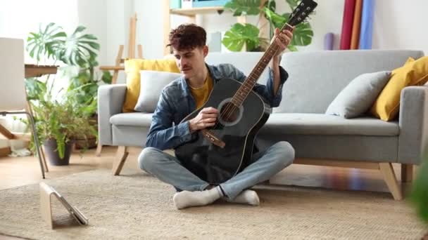 Egy nyugodt, fiatal felnőtt finomhangolja akusztikus gitárját, harmonikus hangulatot teremtve nyugodt otthonában.. - Felvétel, videó