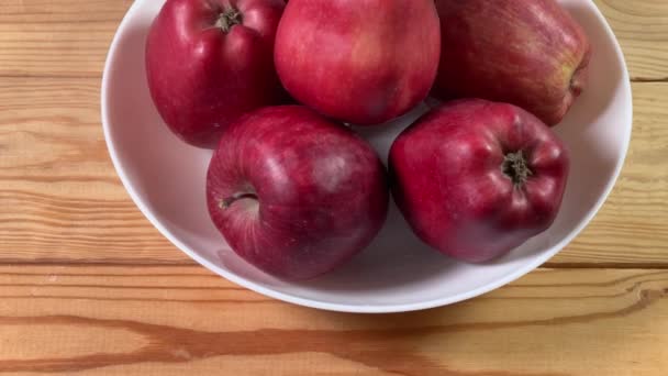Червоні яблука в білій мисці на сільському столі - Кадри, відео