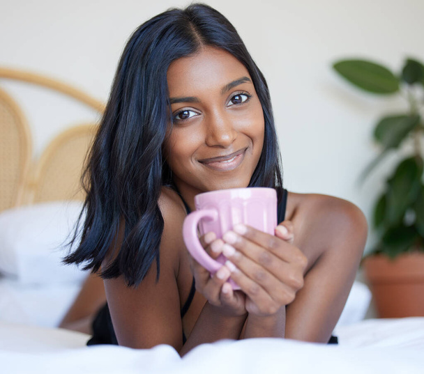 Breakfast, bed and Indian woman with coffee, portrait and smile in morning, relax and happiness in hotel. Vacation, break and holiday for girl, drink and beverage of espresso, resort and bedroom. - Photo, Image