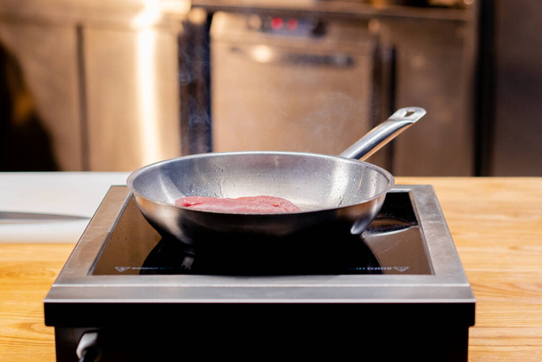 крупным планом сковороды на плите и куском розовой утиной груди на горячей сковороде - Фото, изображение