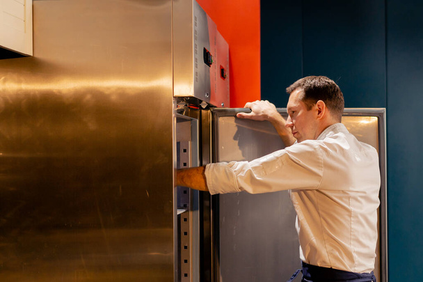 Profi-Küchenchef schaut in Kühlschrank und wählt Zutaten für Kochkonzept - Foto, Bild