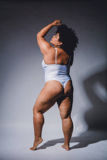 vista posteriore di afrolatina potenziato giovane donna in lingerie in piedi in posa in lingerie bianca su sfondo bianco, studio girato con alto contrasto. - Foto, immagini