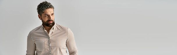 Ein stilvoller Mann mit verführerischem Bart posiert selbstbewusst in eleganter Kleidung vor einem glatten weißen Hintergrund. - Foto, Bild