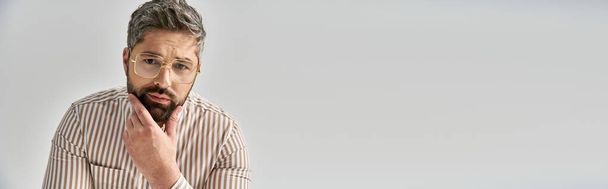 Stylový muž s vousy a elegantním oblečením vypadá překvapeně ve studiu nastavení na šedém pozadí. - Fotografie, Obrázek