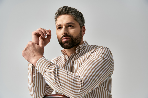 A stylish man with a beard strikes a pose in a striped shirt against a gray studio backdrop. - Photo, Image