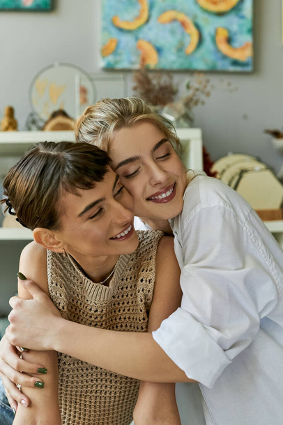 Dwie kobiety, kochająca lesbijska para, dzielą czuły uścisk w pracowni artystycznej. - Zdjęcie, obraz