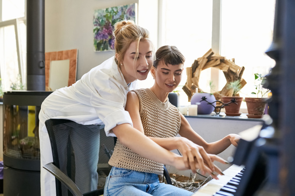 Μια γυναίκα κάθεται με την κοπέλα της σε ένα πιάνο, μοιράζονται μια μουσική στιγμή. - Φωτογραφία, εικόνα